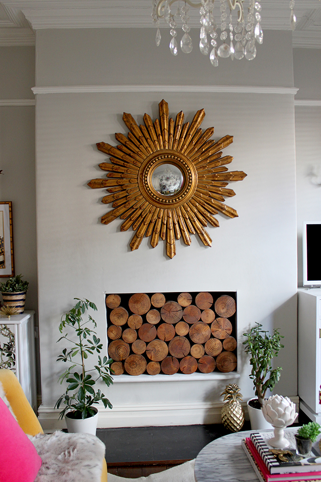 Swoon Worthy living room - gold star burst mirror, grey walls, decorative logs in fireplace