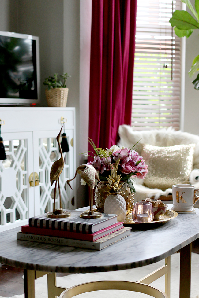 coffee table styling - brass cranes, marble coffee table, pink flowers, white and gold pineapple, brass tray, pink candle - see more on www.swoonworthy.org