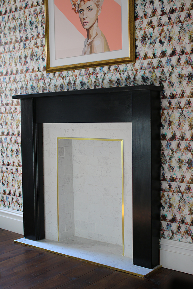 marble tile fireplace with brass trim and black hearth with graphic wallpaper - see the whole process on www.swoonworthy.org