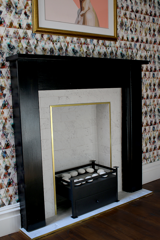 marble tile fireplace with brass trim and black hearth with graphic wallpaper - see the whole process on www.swoonworthy.org