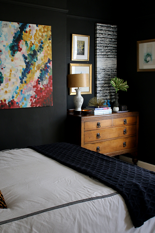 black bedroom with vintage dresser and bright colourful art - see more on www.swoonworthy.org