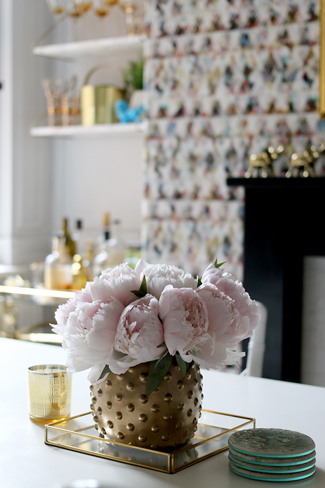 vase of peonies in dining room with graphic wallpaper, black fireplace mantle, gold accents - see more on www.swoonworthy.org