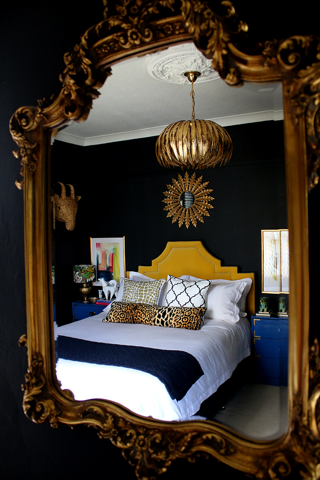 black bedroom with gold light fixture, yellow headboard and colourful artwork - see more on www.swoonworthy.org