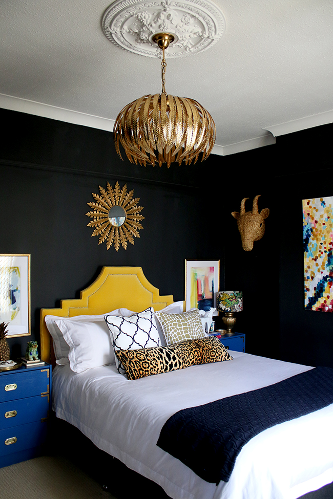 black bedroom with gold light fixture, yellow headboard and colourful artwork - see more on www.swoonworthy.org