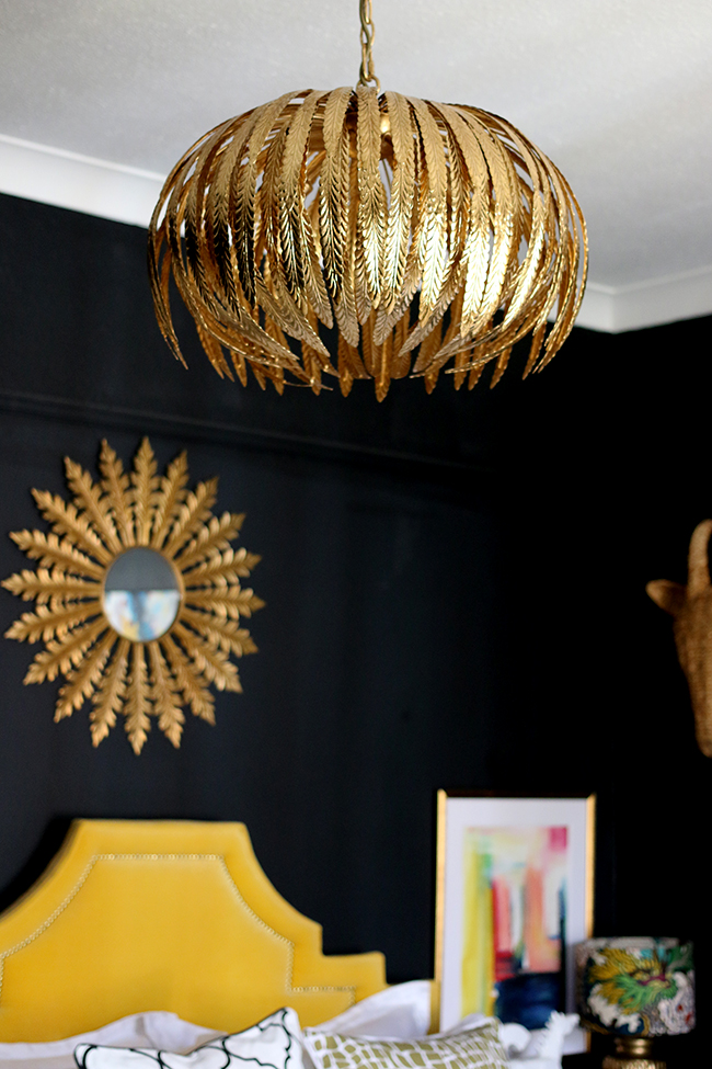 black bedroom with gold light fixture, yellow headboard and colourful artwork - see more on www.swoonworthy.org