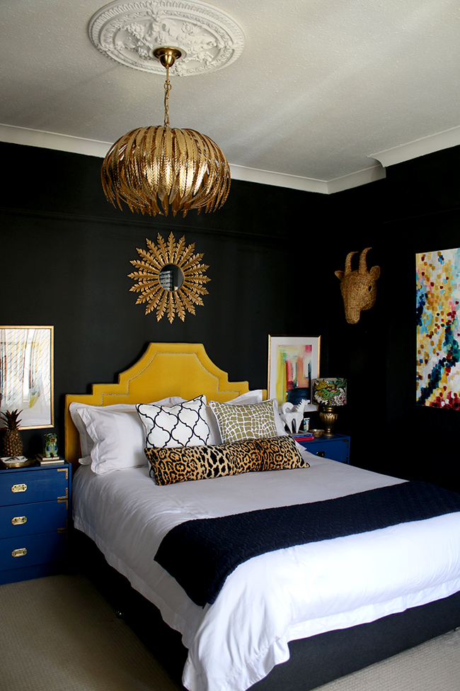 black bedroom with gold light fixture, yellow headboard and colourful artwork - see more on www.swoonworthy.org