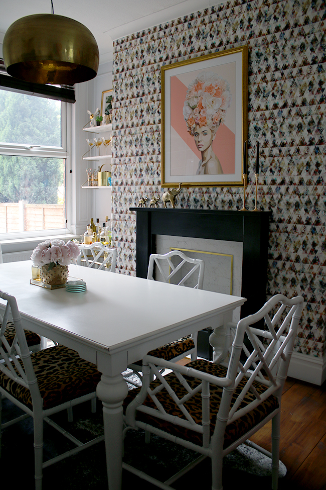 Eclectic glam dining room with graphic feature wallpaper, leopard print chairs, black and marble fireplace and gold light fixture