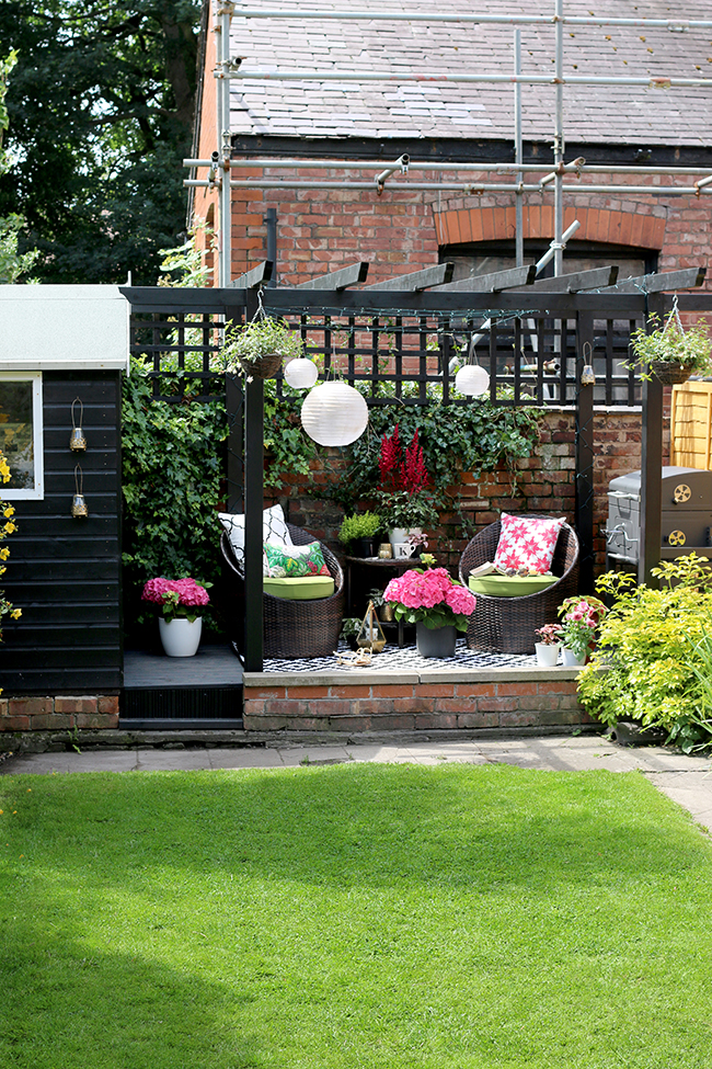 black shed and pergola patio area with hanging lanterns in pink and green