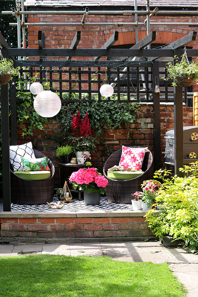 English garden with black pergola and decking area in pink and green