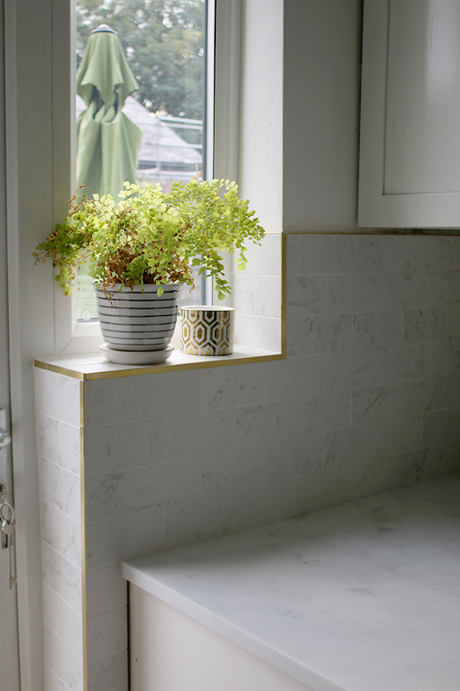 Marble effect porcelain tiles with brass trim work along windowsill in the kitchen