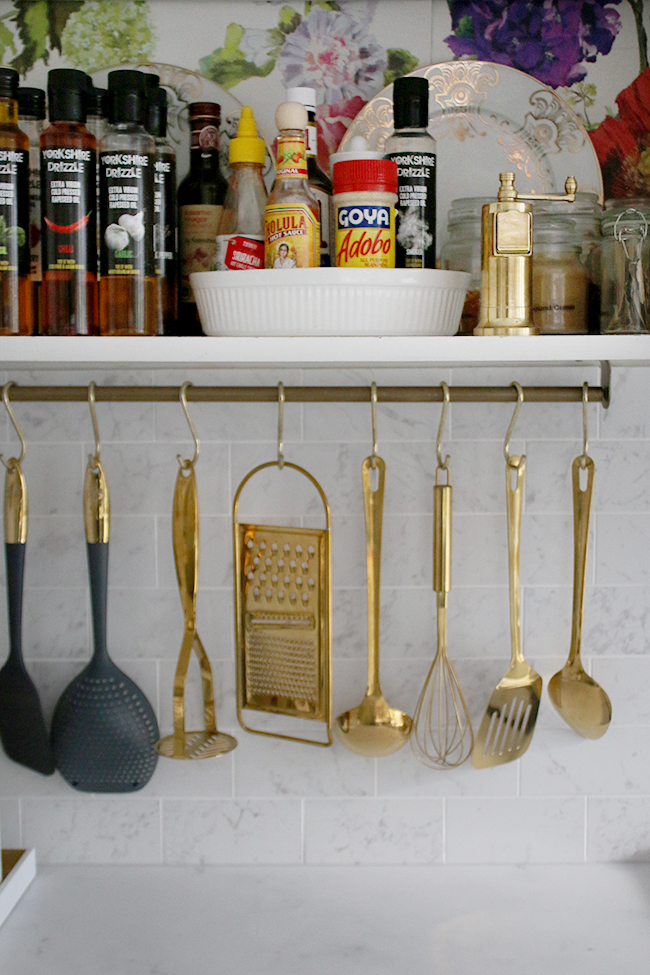 Marble effect kitchen tiles with gold hanging utensils and open storage in the kitchen