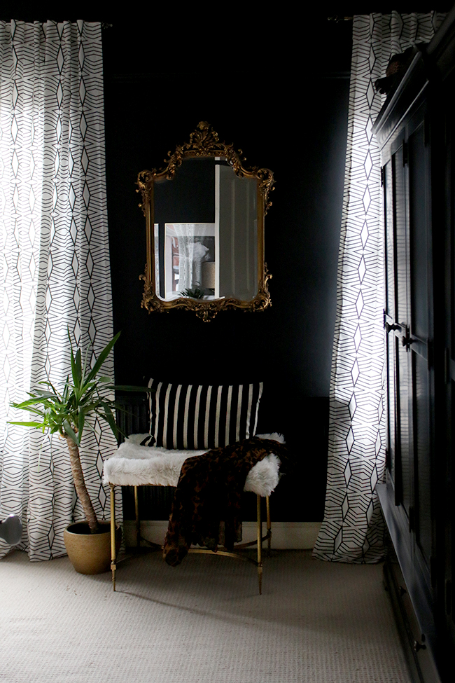 black walls with ornate mirror and brass bench with patterned curtains