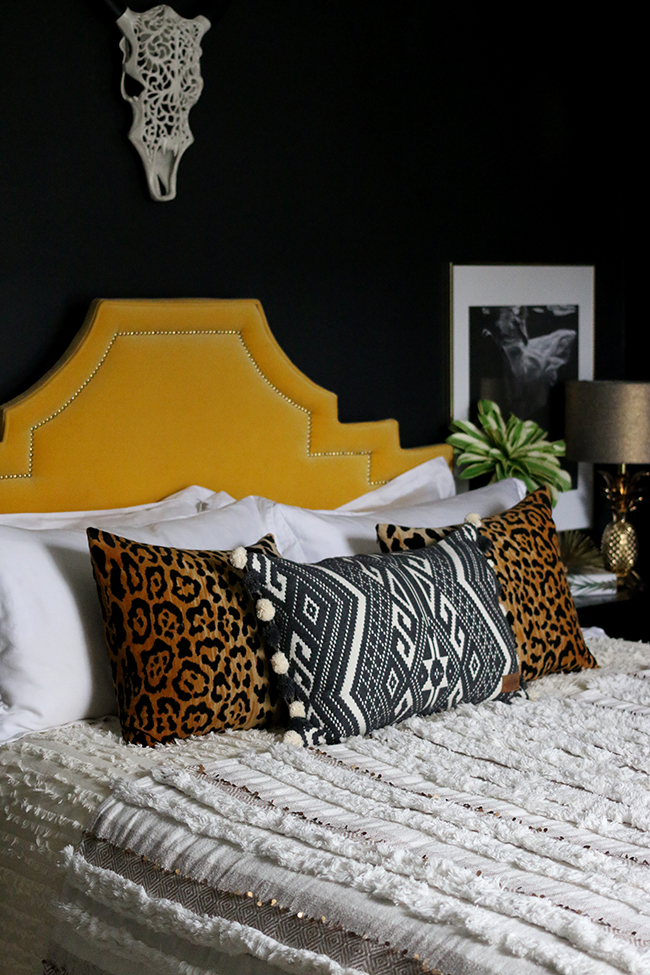 moroccan style wedding blanket with leopard print cushions in black bedroom with yellow headboard