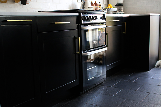 black kitchen cabinets with gold hardware and slate flooring