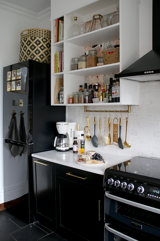 kitchen with black cupboards with white open shelving, marble tiles and brass accents