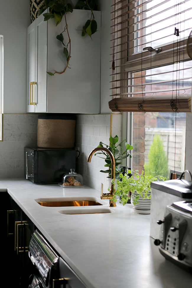 kitchen with black cupboards with white open shelving, marble tiles, gold sink and gold tap