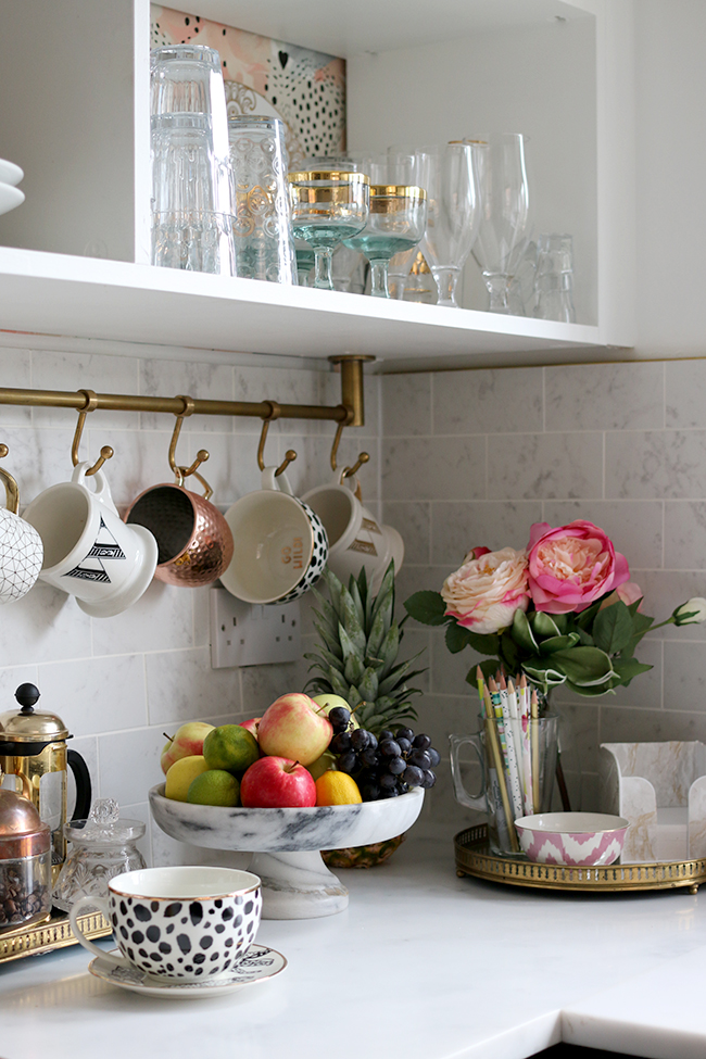 kitchen corner with marble tiles, brass rail with cups and fruit bowl