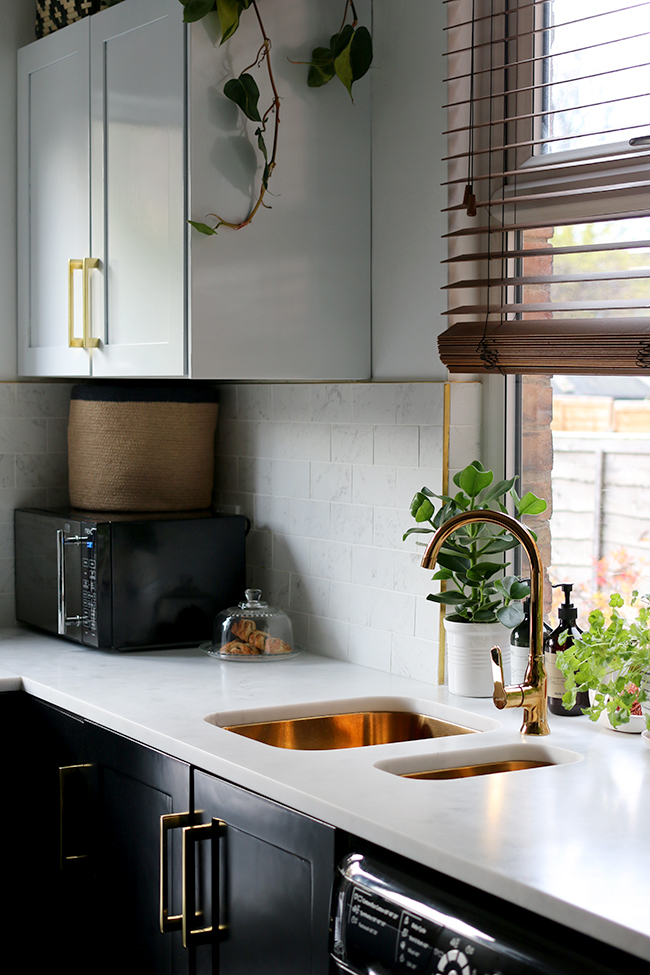 kitchen with black cupboards with white open shelving, marble tiles, gold sink and gold tap