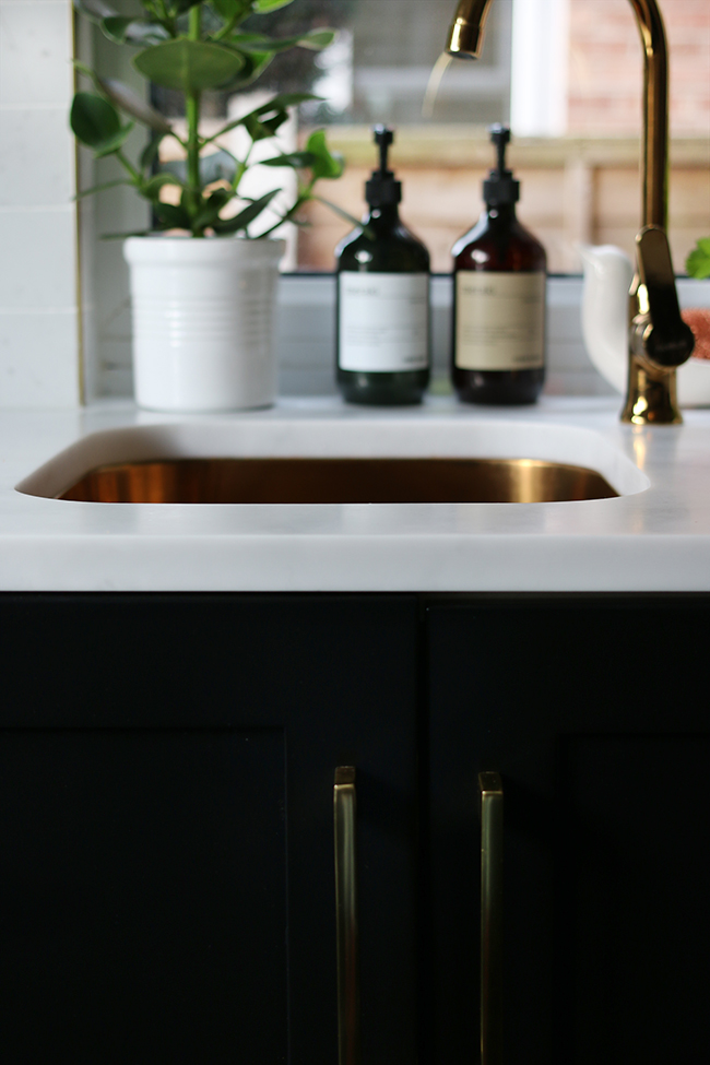 black lowers with marble effect countertop and gold sink and faucet