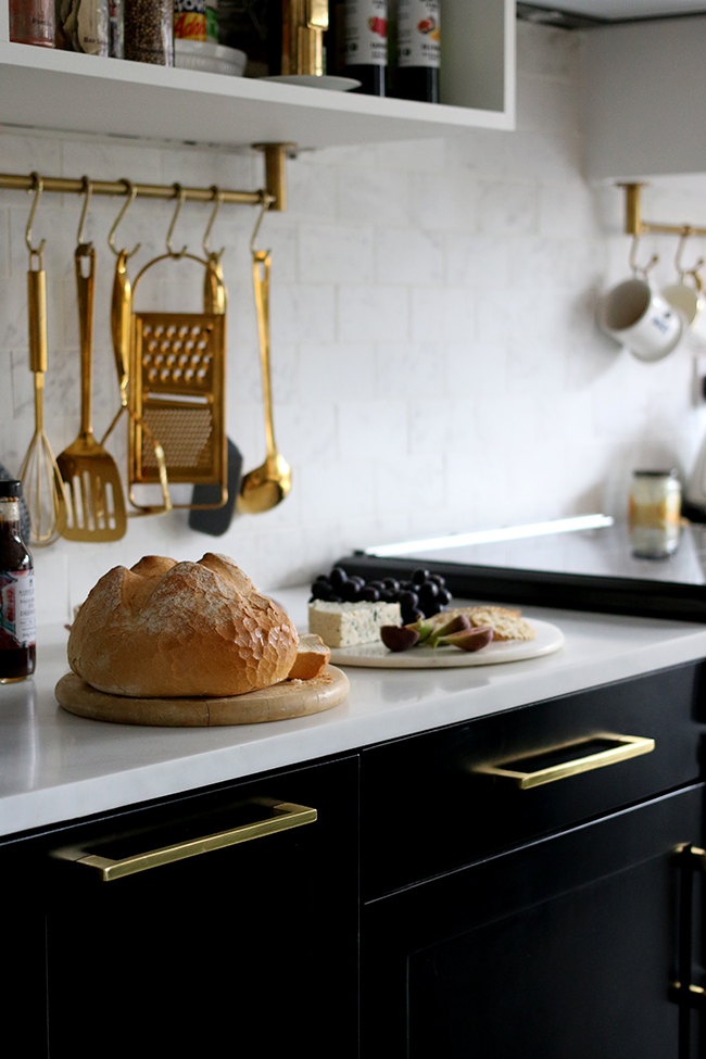 marble effect tiles and countertop with black kitchen cabinets and gold cabinet handles and gold hanging utensils