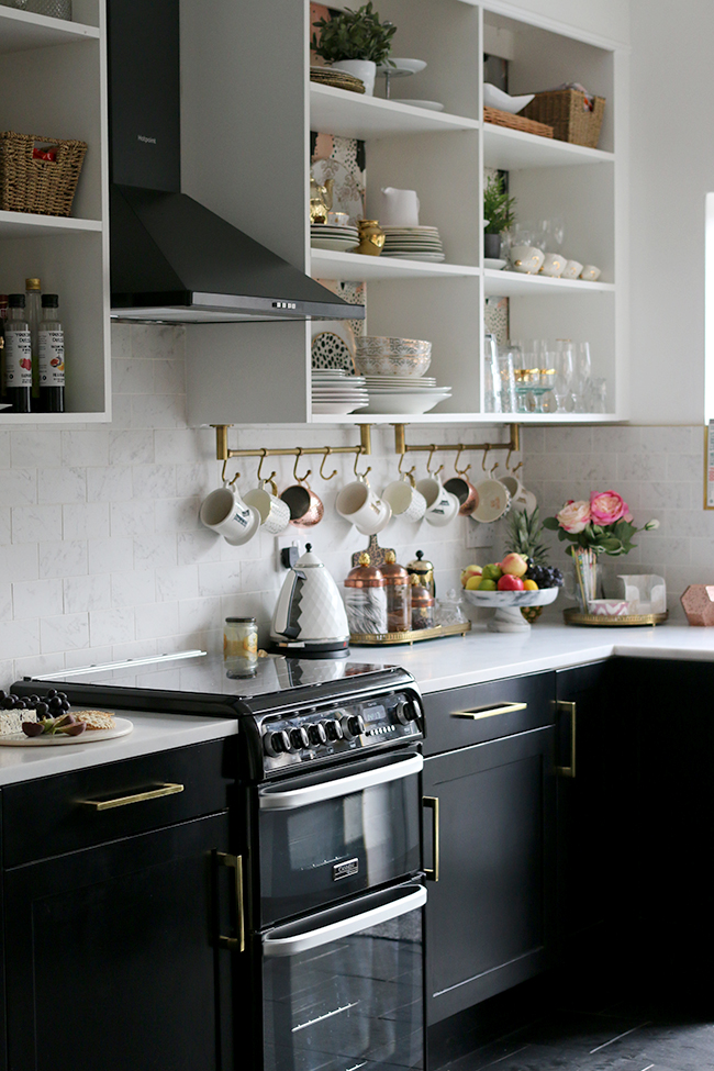 kitchen with black cupboards with white open shelving, marble tiles and brass accents