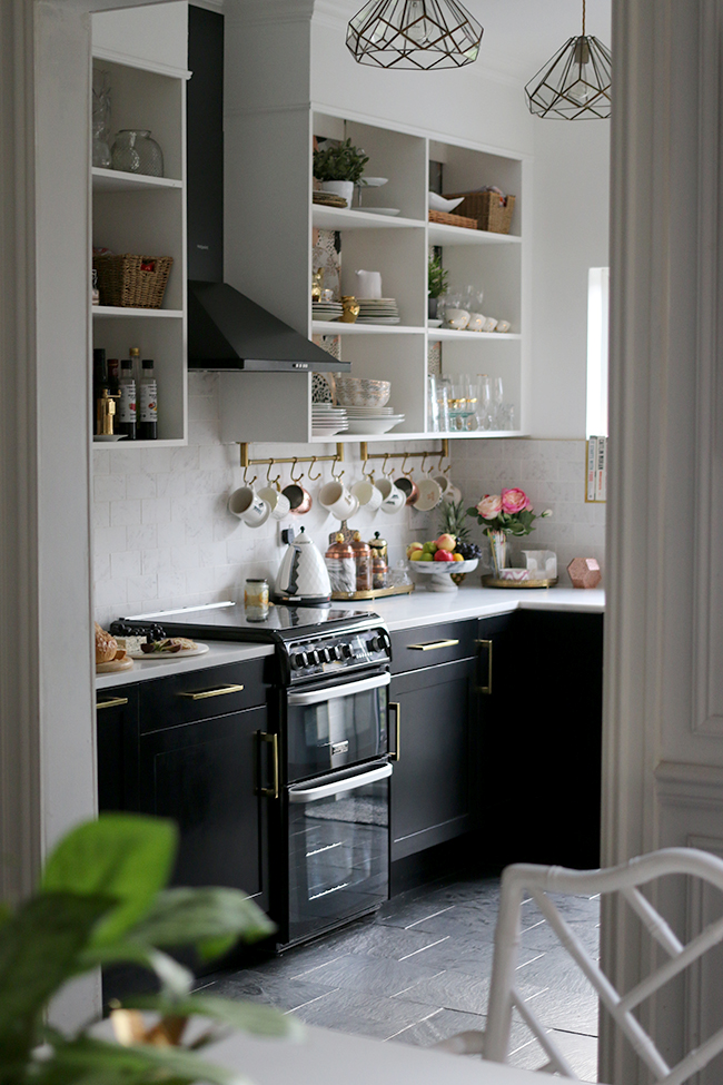 kitchen with black cupboards with white open shelving, marble tiles and brass accents