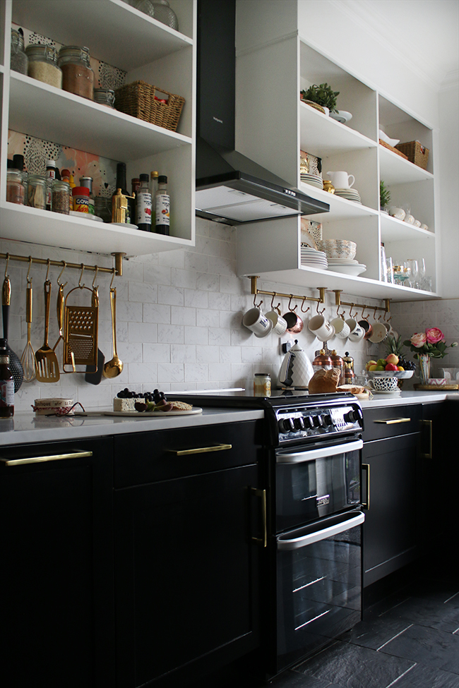 Black, white and gold kitchen with slate floors and white open shelving with brass details