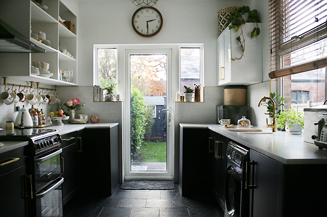 black white and gold kitchen with slate floors, black lowers and white open shelving with brass details and gold faucet