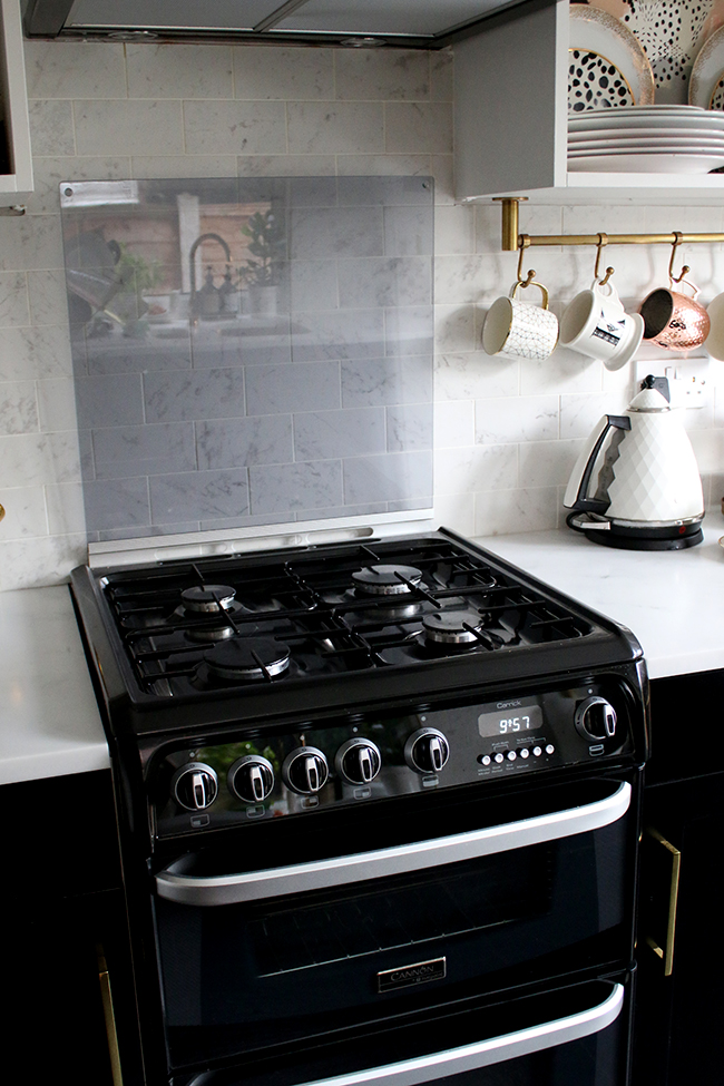 Black oven with flip up splashback screen with black cupboards and gold hardware in kitchen