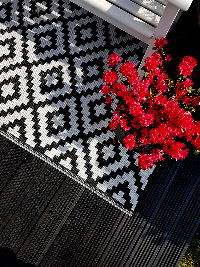 black decking with black and white outdoor rug and pink azaleas