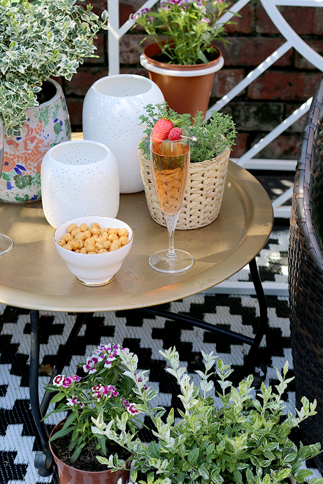 gold table with black and white outdoor rug and white candle lanterns from West Elm