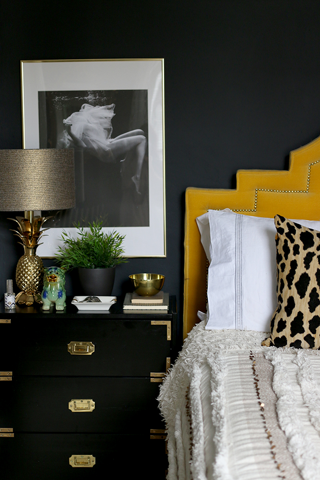 black bedroom with black and white photography art, black campaign style ikea nightstand and yellow headboard