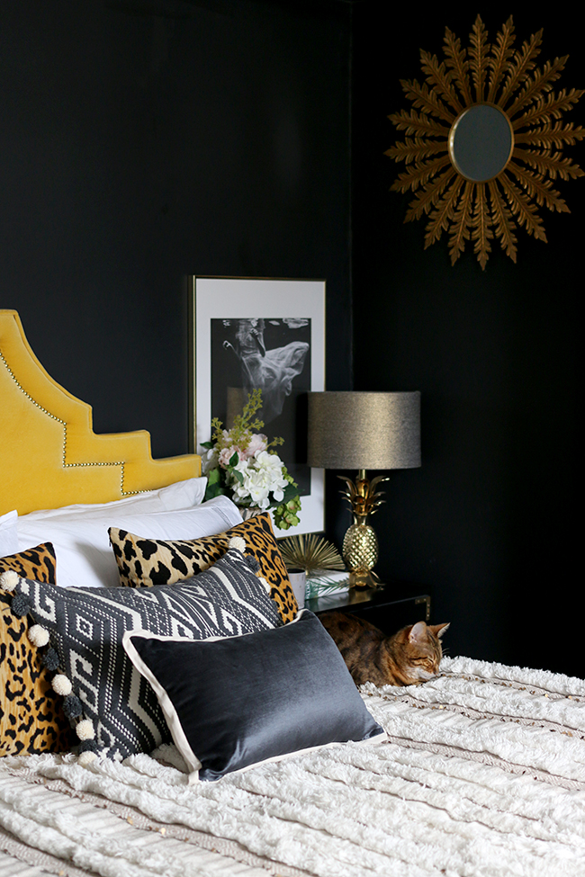 black bedroom with yellow velvet headboard leopard print cushions and gold pineapple lamp