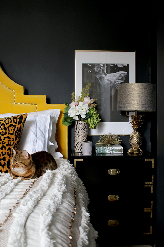 black bedroom with yellow velvet headboard leopard print cushions and gold pineapple lamp