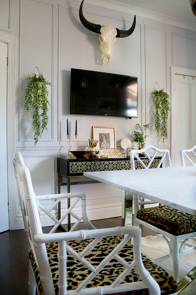 grey dining room with black and gold console and TV on wall