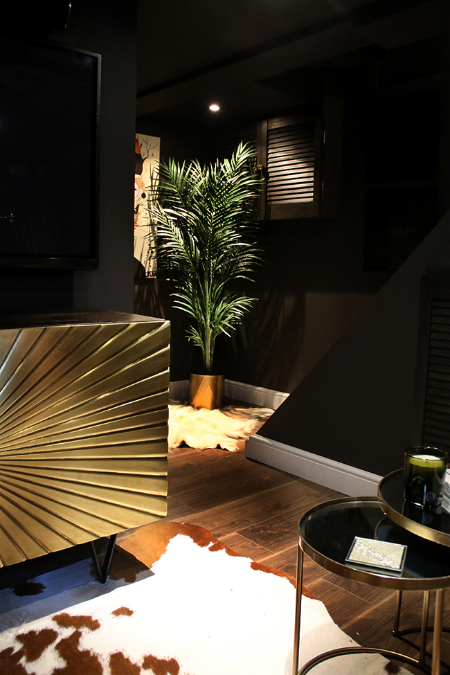 black room with gold sideboard and faux plant in corner